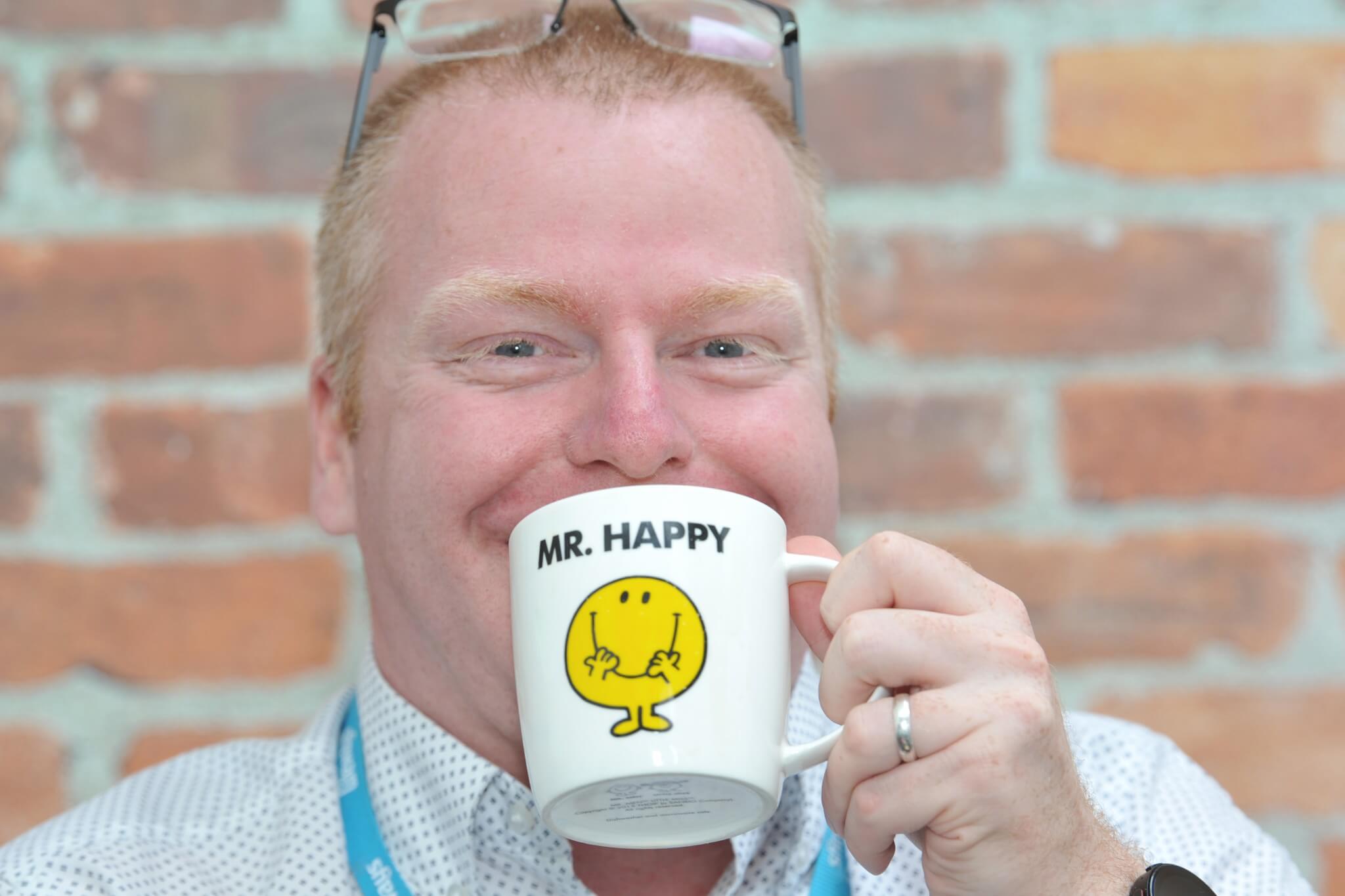 Man smiling with a Mr Happy mug