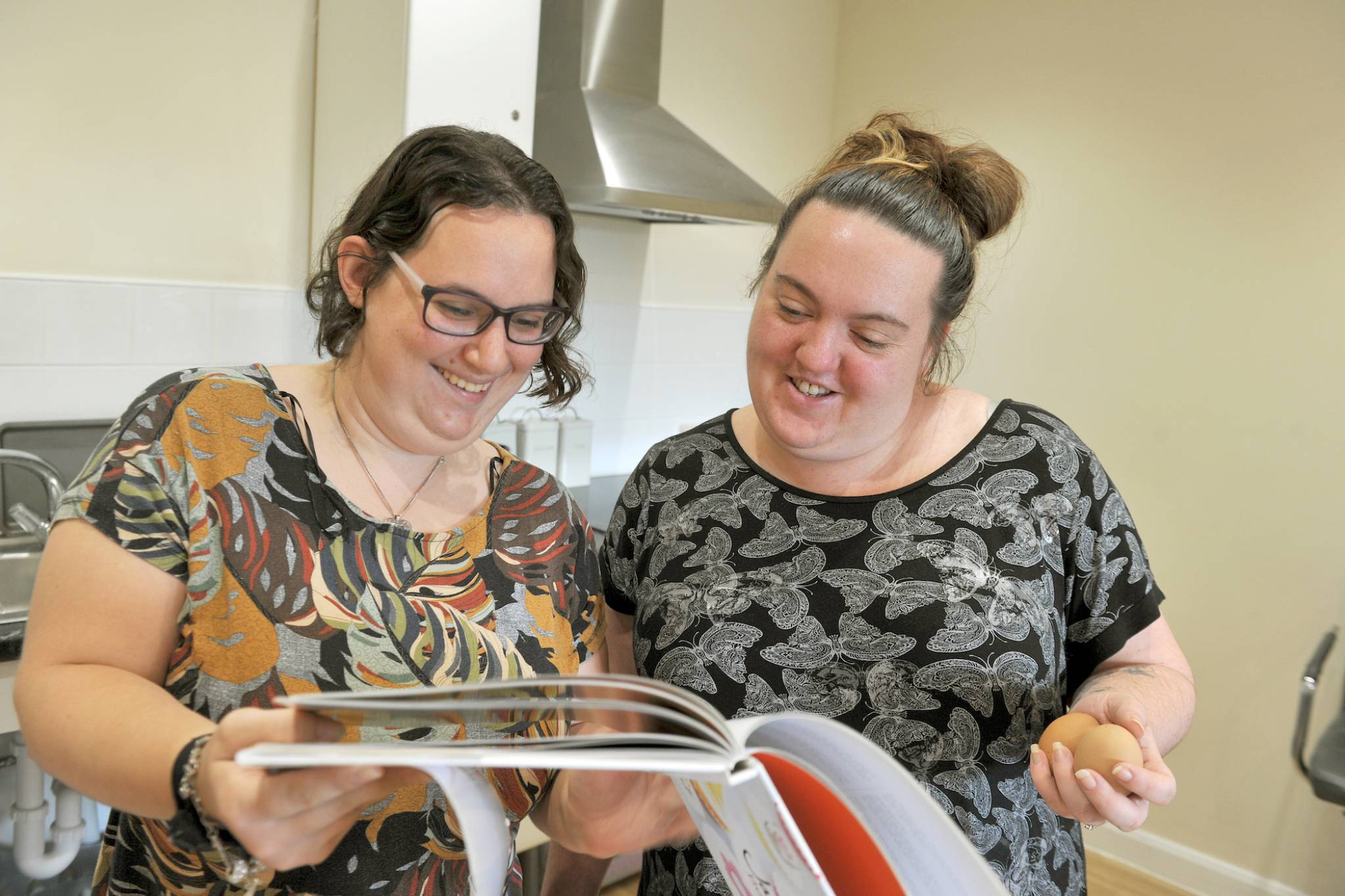 Two woman reading cookbook whilst smiling