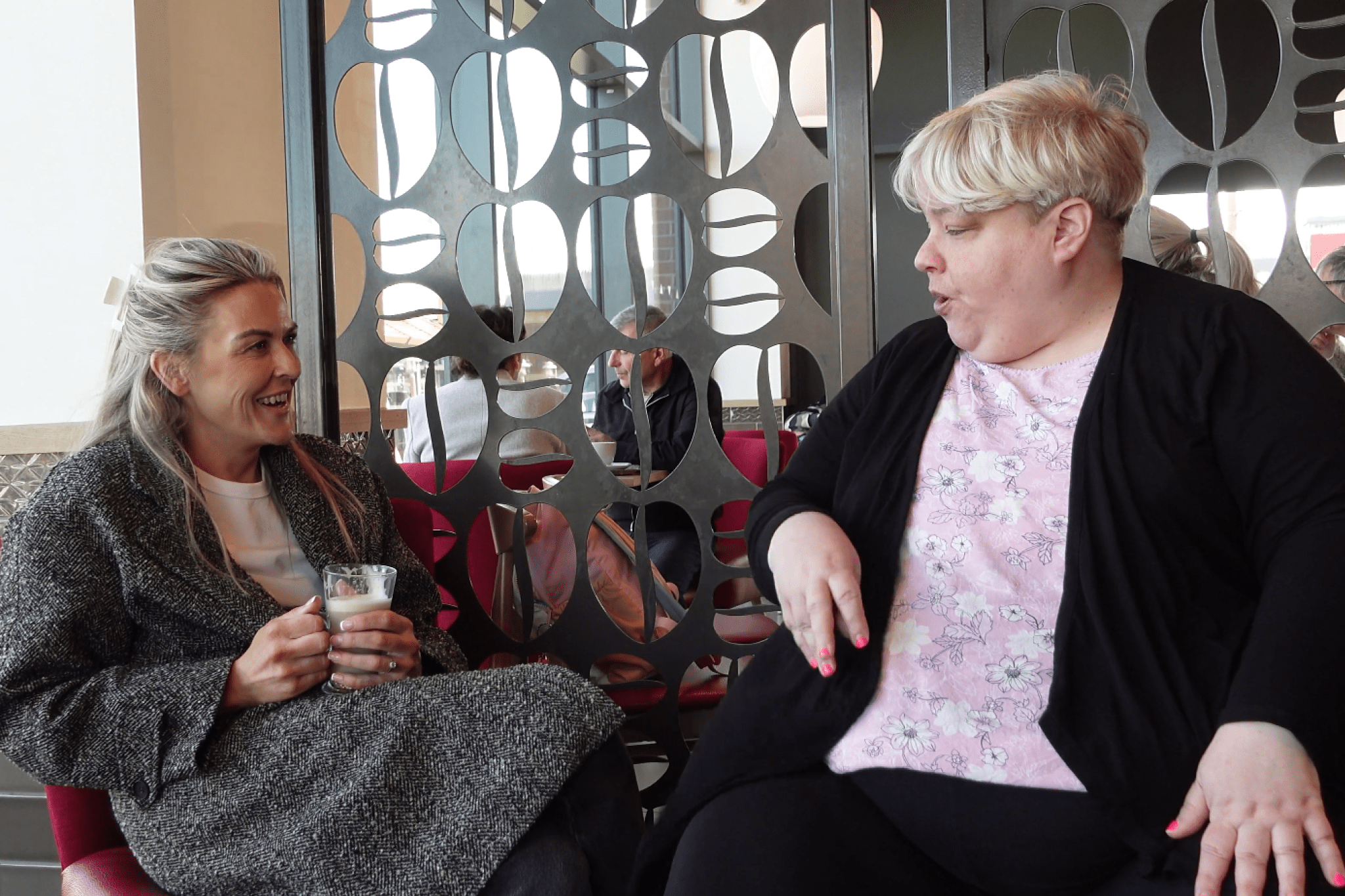 A smiling support worker is sitting with a person we support in a coffee shop